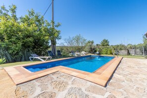A rectangular swimming pool with tiled edges, surrounded by stone tiles and a grassy area.