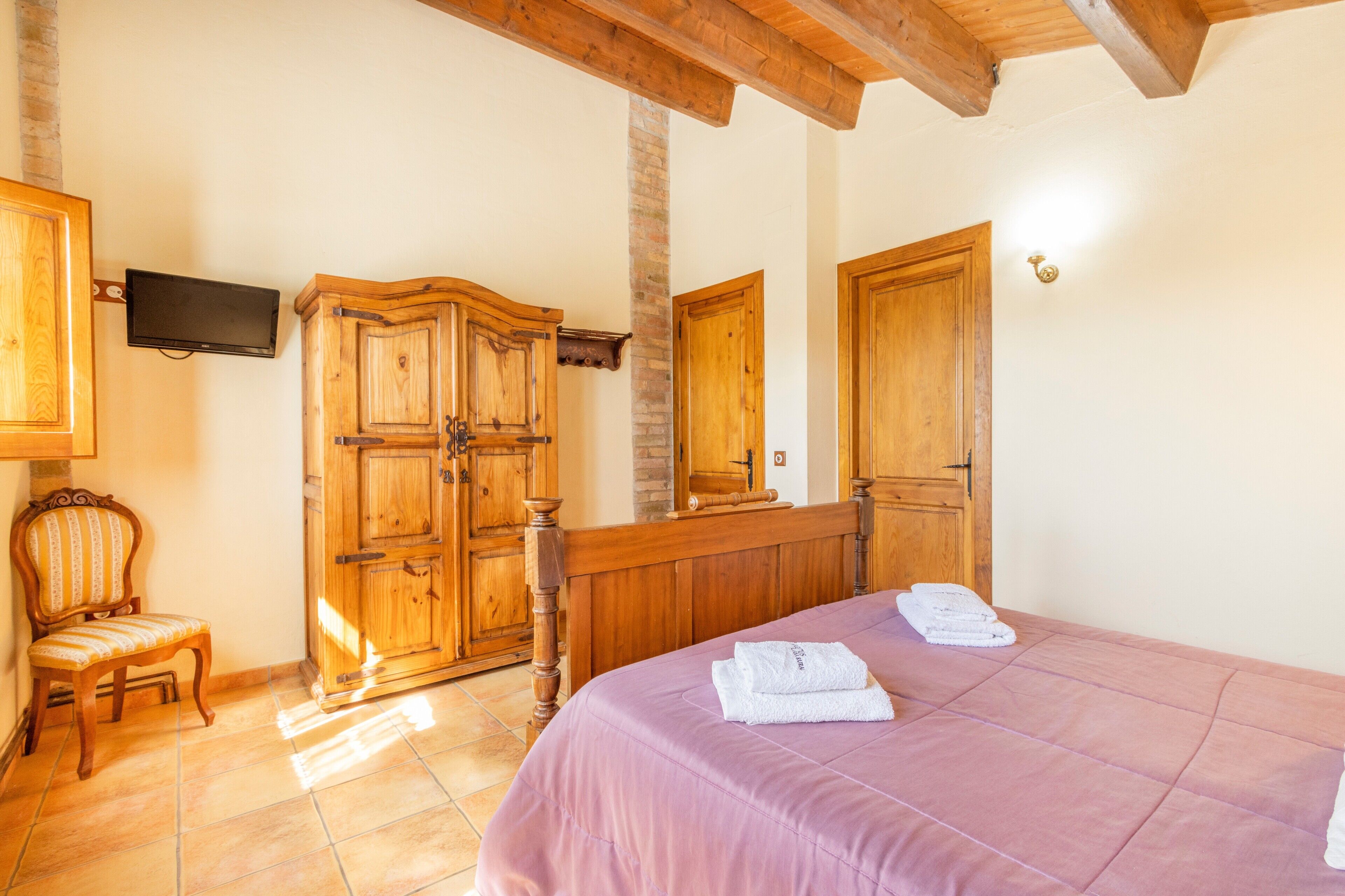 Un dormitorio con cama, armario de madera, una silla y televisor en la pared.