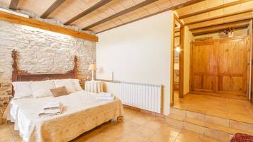 A bedroom with a stone wall, wooden ceiling beams, a bed with a quilt, a radiator, and a wooden door.