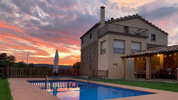 Una piscina con un borde de baldosas, una valla de madera y un edificio con balcón.