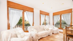 Una habitación con un conjunto de sofás, una mesa de madera y ventanas grandes con cortinas.