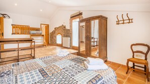 Un dormitorio con una cama, una silla de madera, una mesa de madera, un espejo y una pared de piedra.