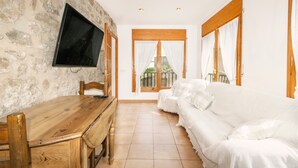 Una habitación con pared de piedra, muebles de madera, televisión, cama y vista por una puerta.