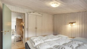 Et soveværelse med en stor seng, trævægge og en dør til en opholdsstue.