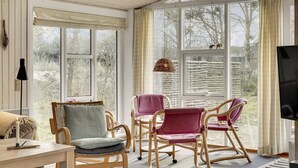 Et hyggeligt værelse med fletstole, et bord med et stearinlys og store vinduer med udsigt til det fri.
