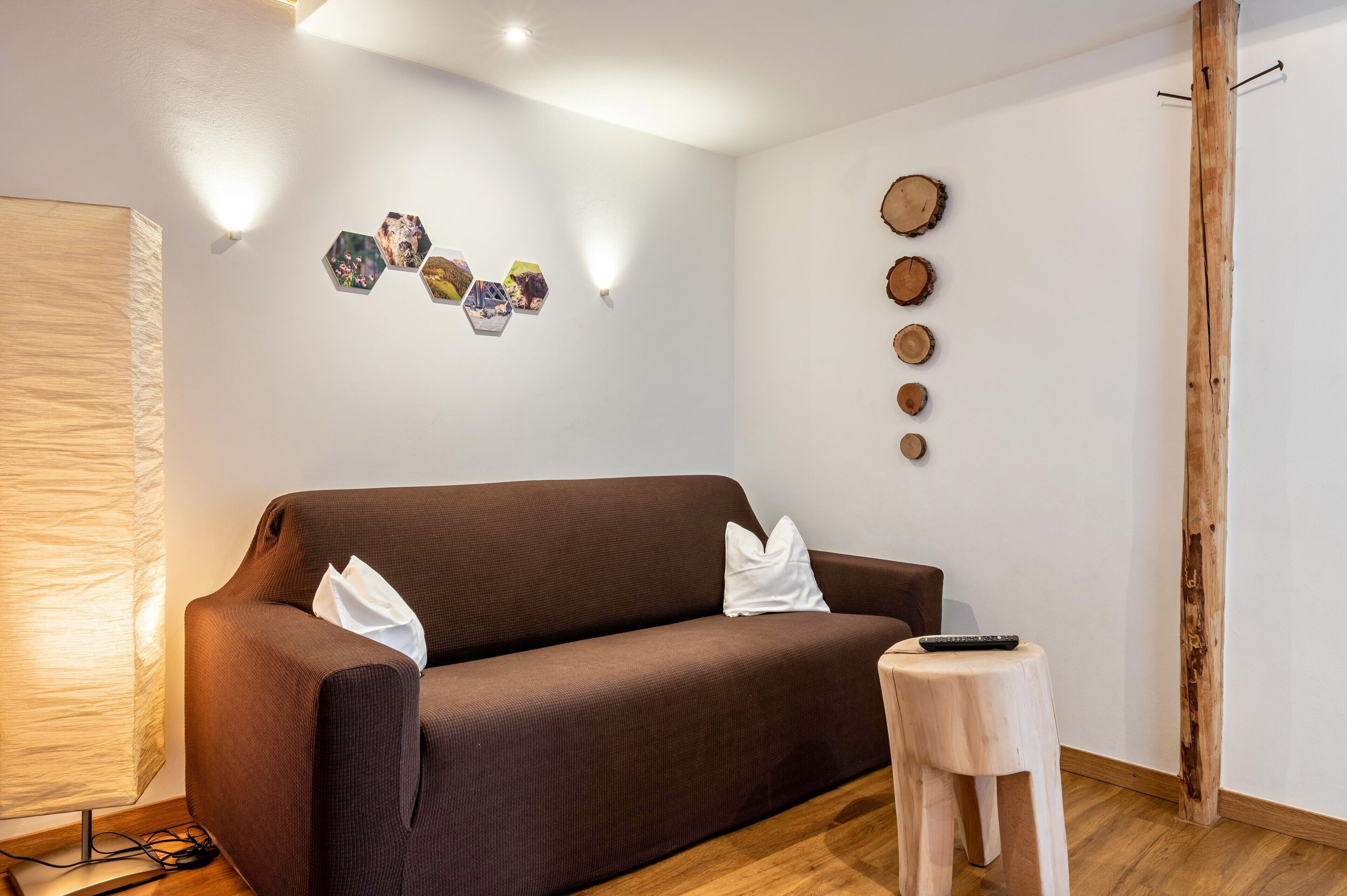 Een moderne woonkamer met een bruine bank, een klein houten krukje en een wandlamp.