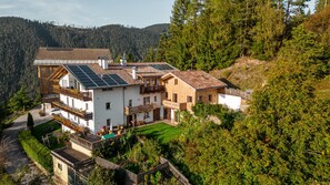 A multi-story chalet with solar panels, a balcony, and a view of a forested valley.