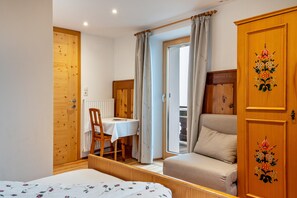 Une pièce comprenant un lit, une armoire en bois, une table avec une chaise et une fenêtre avec des rideaux.