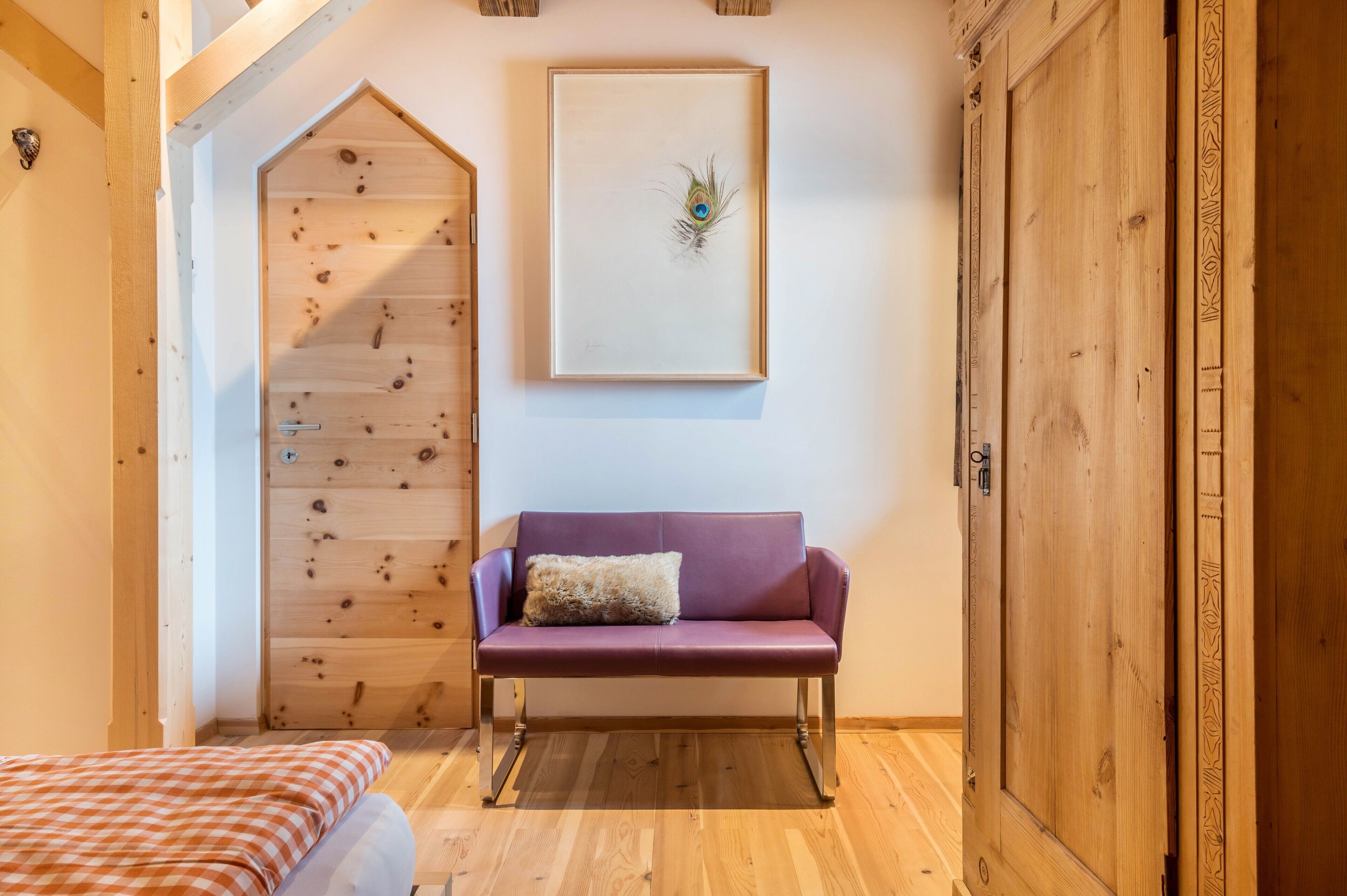 Ein Zimmer mit schrägem Holzboden, einem violetten Sofa mit Kissen, einem gerahmten Kunstwerk an der Wand und einem Holzschrank.