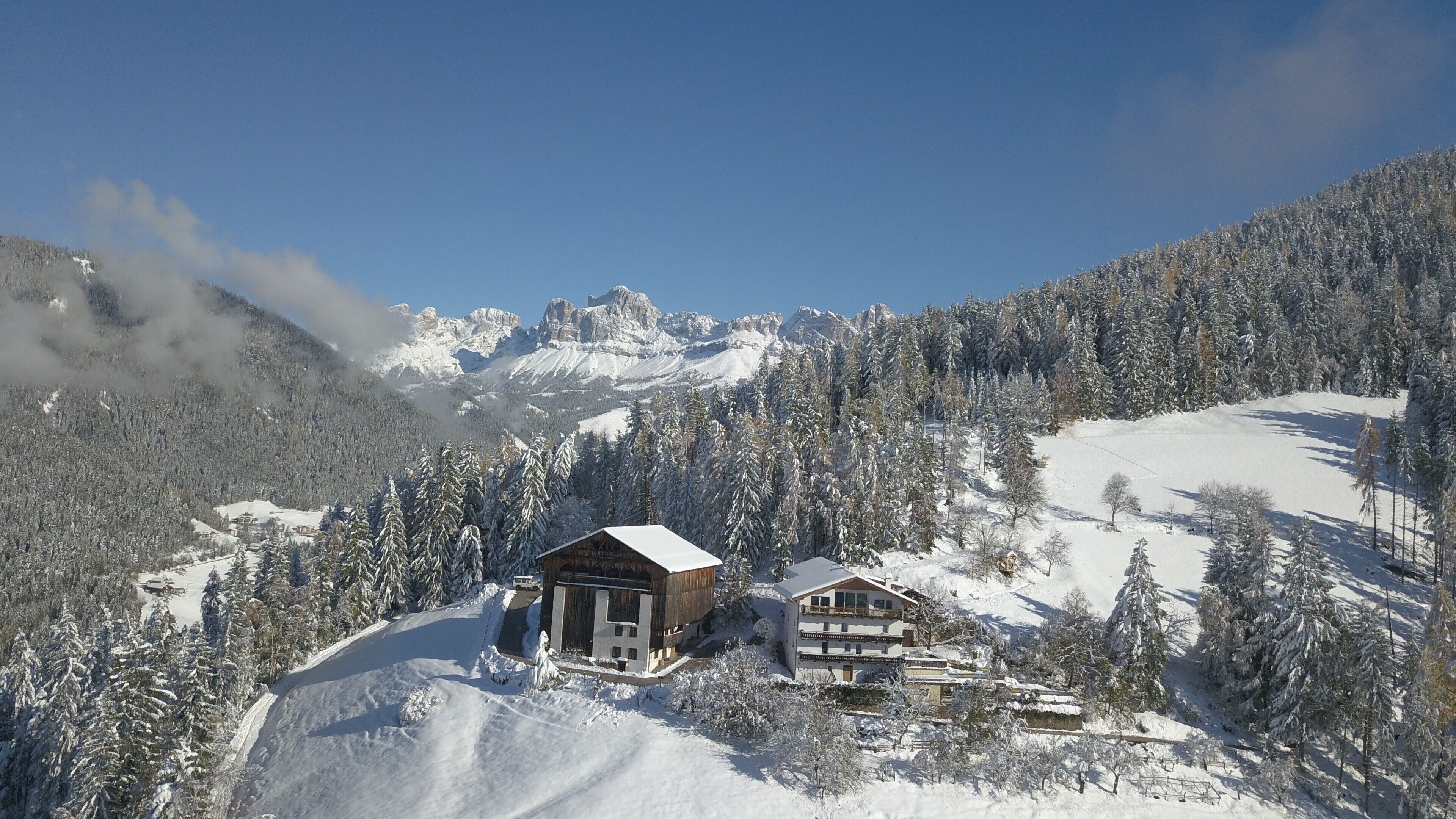 Paisagem montanhosa coberta de neve com duas cabanas de madeira e um teleférico ao fundo.