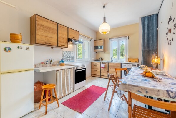 Une cuisine avec des meubles de rangement en bois, un réfrigérateur blanc, une cuisinière, une table à manger avec des chaises et un tapis rouge.