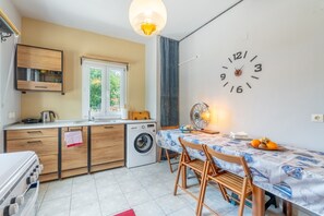 Une cuisine compacte équipée d’un lave-linge, de meubles en bois, d’une table à manger avec des chaises et d’une horloge murale.