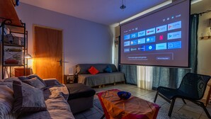 Olohuoneessa on sohva, sohvapöytä, televisioruutu, jossa näkyy sovellusten kuvakkeita, ja kirjahylly.