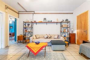 Une pièce comprenant un canapé, une table avec un saladier, une bibliothèque et une porte.