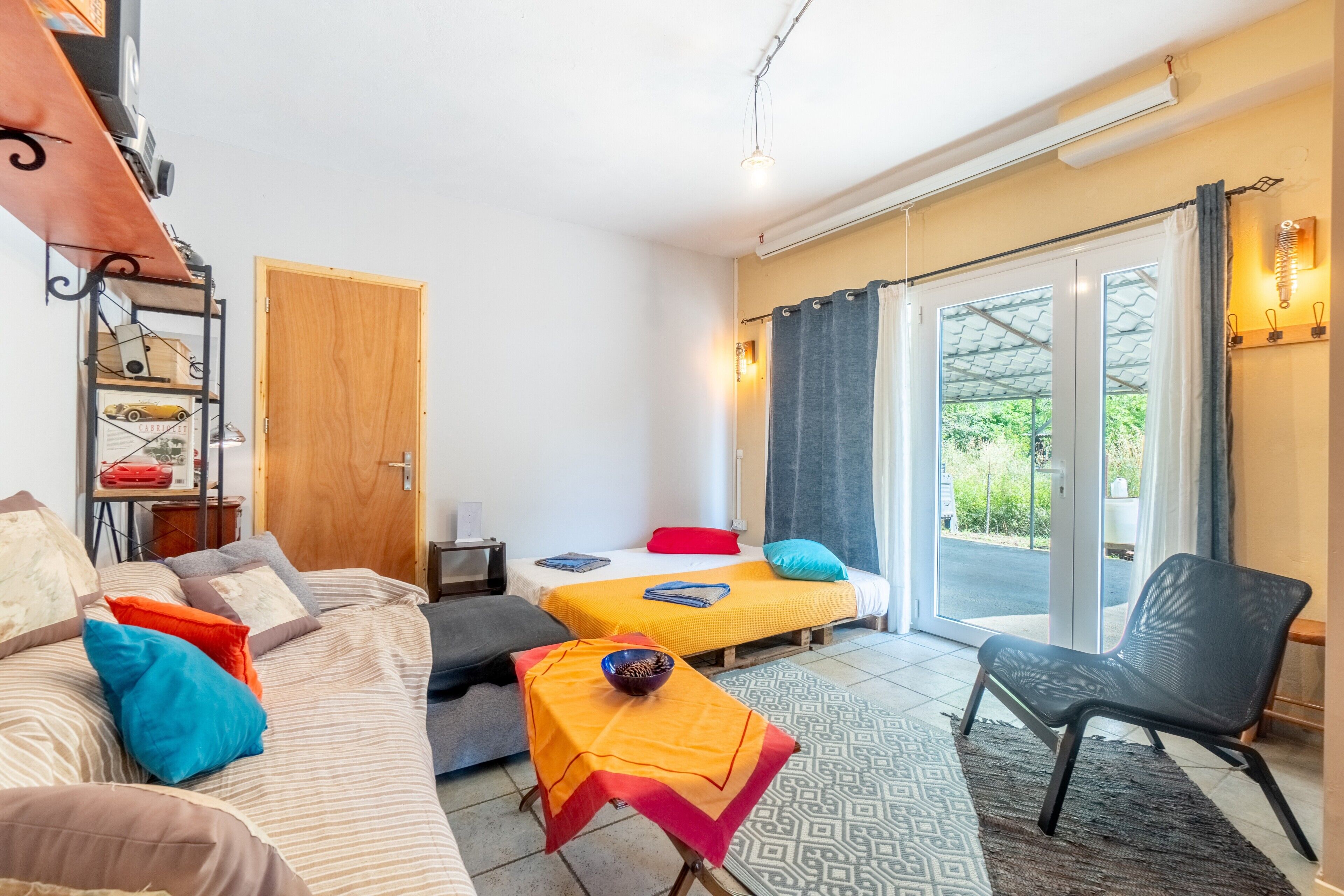 Une chambre avec deux lits, un canapé, une chaise, une petite table avec un bol, et une porte donnant sur un balcon.