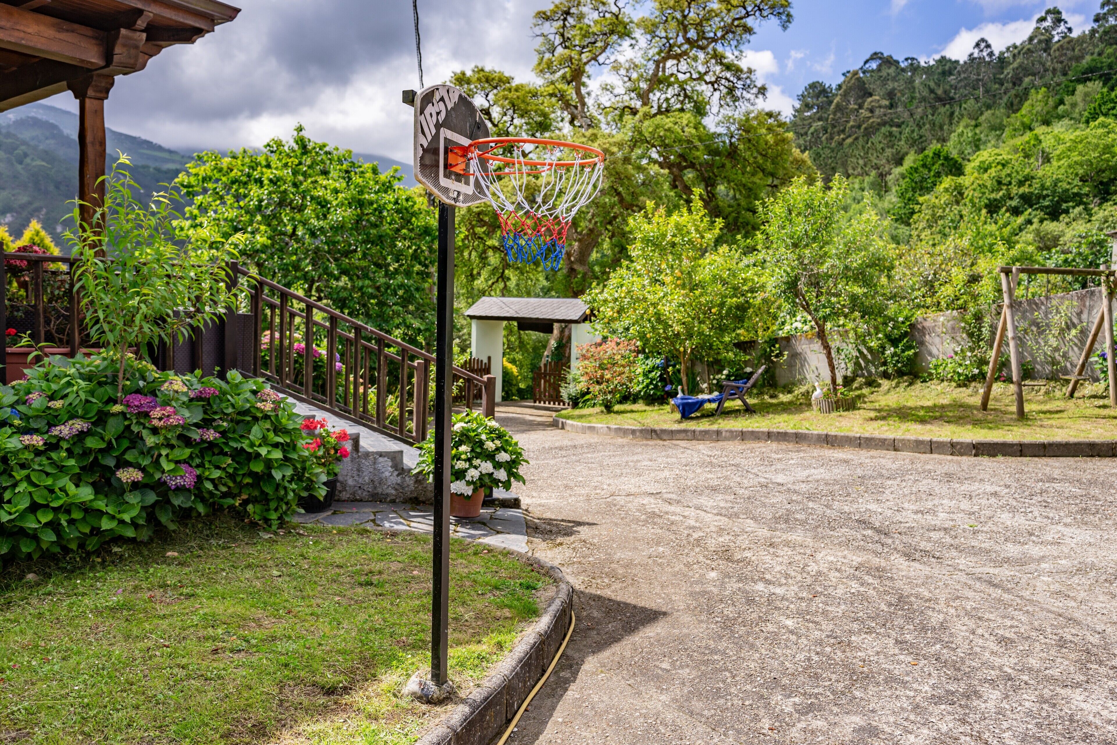 Basketballplatz mit Korb, umgeben von Grünflächen und einer Bergkulisse.