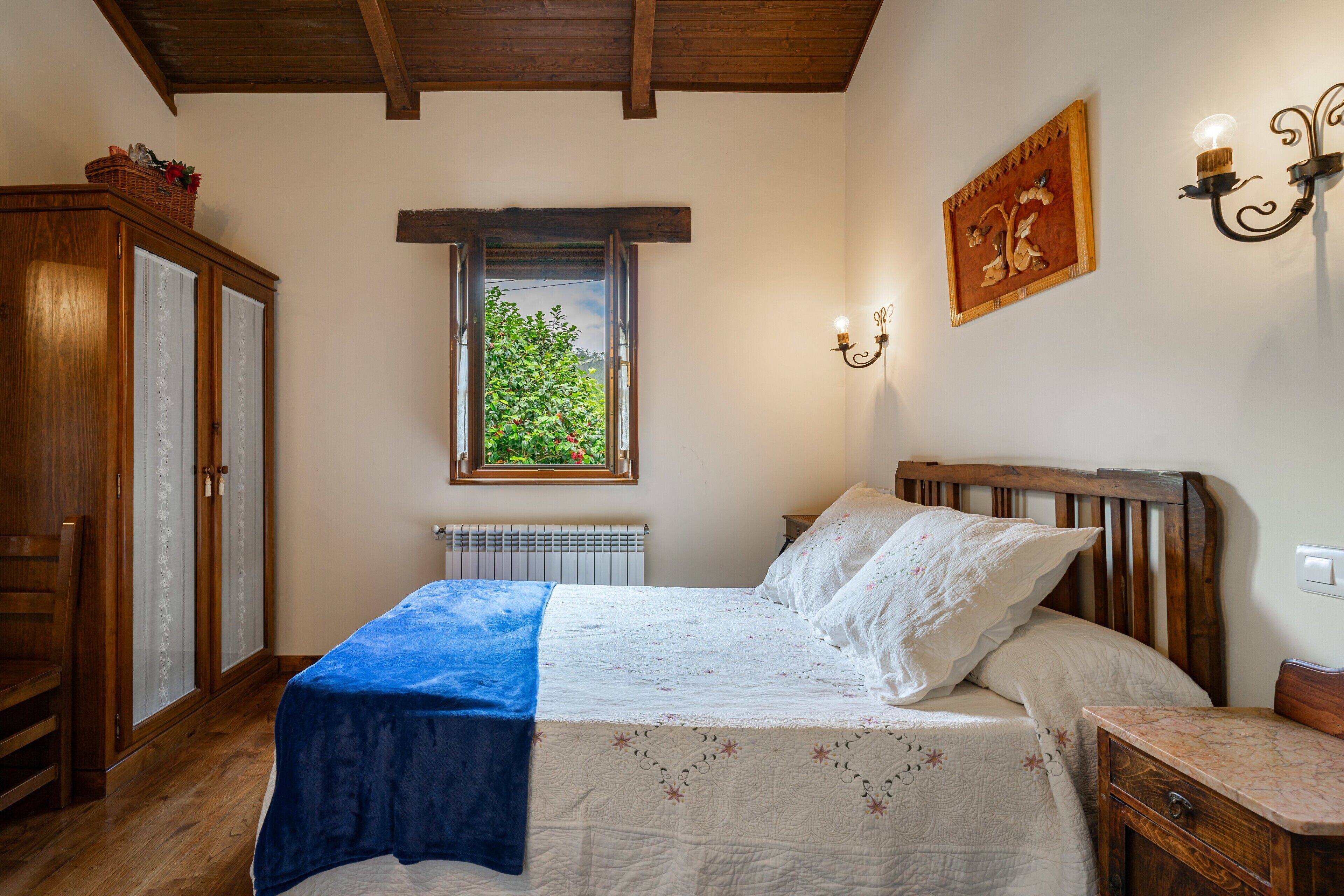 A bedroom with a bed, a window, a radiator, a wooden wardrobe, and a wall-mounted light fixture.