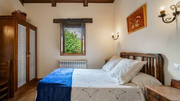 A bedroom with a bed, a window, a radiator, a wooden wardrobe, and a wall-mounted light fixture.