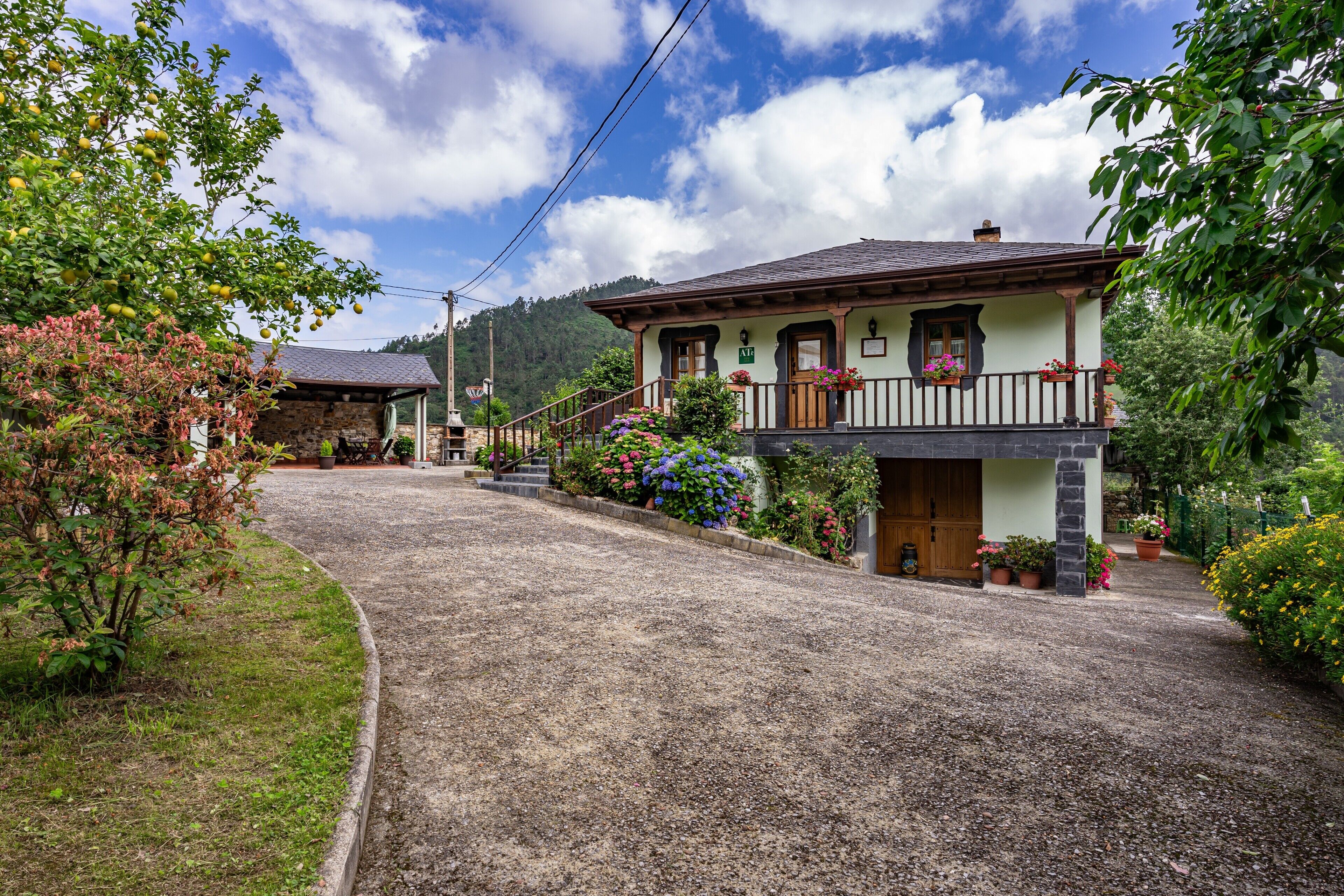 A traditional chalet-style building with a stone facade, a wooden balcony with flower boxes, and a gravel driveway.