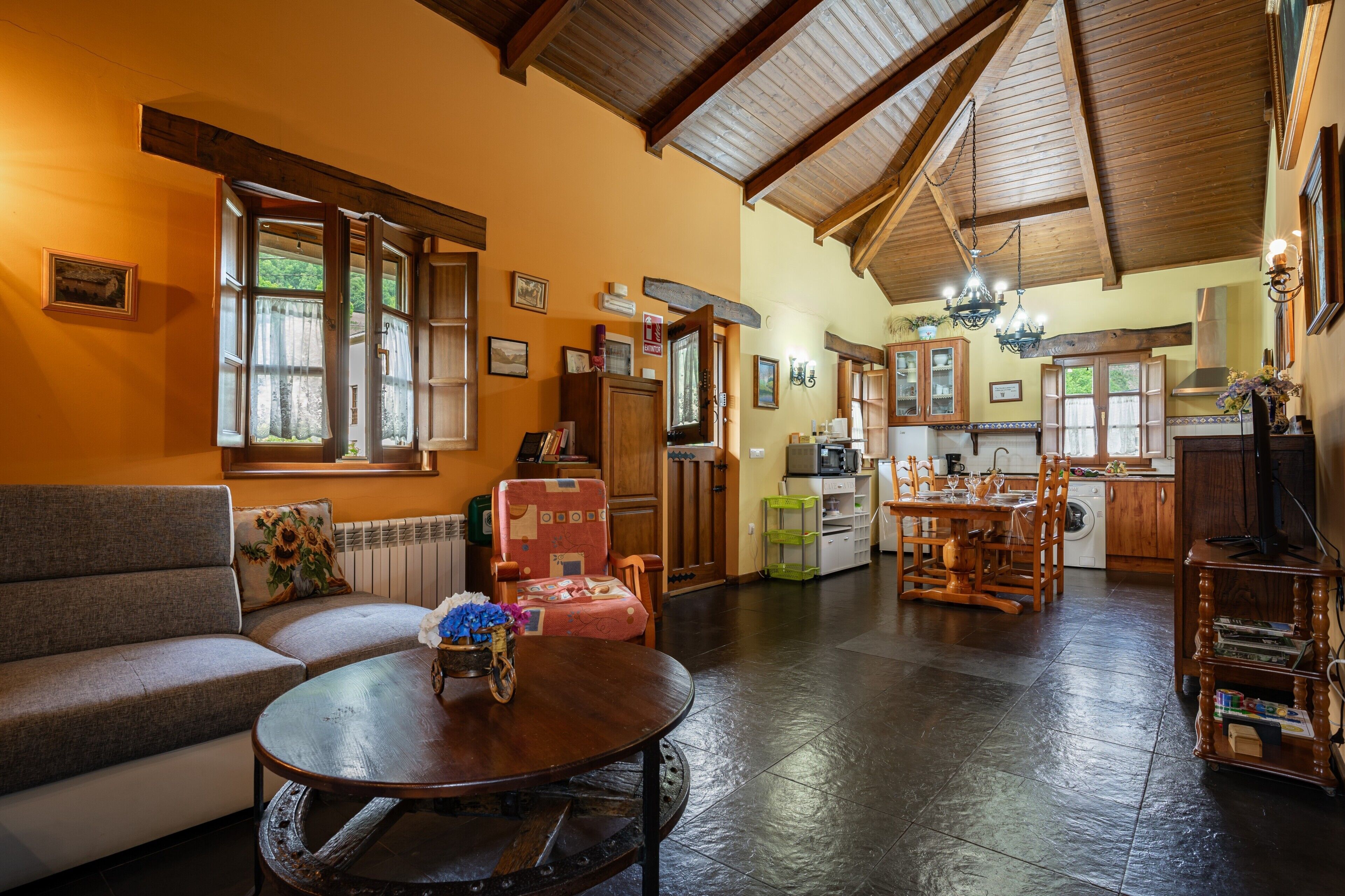 Una sala de estar acogedora con un sofá, una mesita redonda y un comedor con una mesa y sillas de madera.