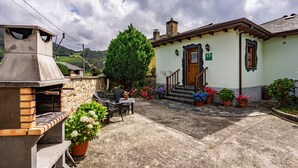 A building with a chimney, a wooden door, and a sign that reads 'AT'. - Holiday Home 'Maseda 2' with Mountain Views, Shared Terrace & Private Garden (Villayon)