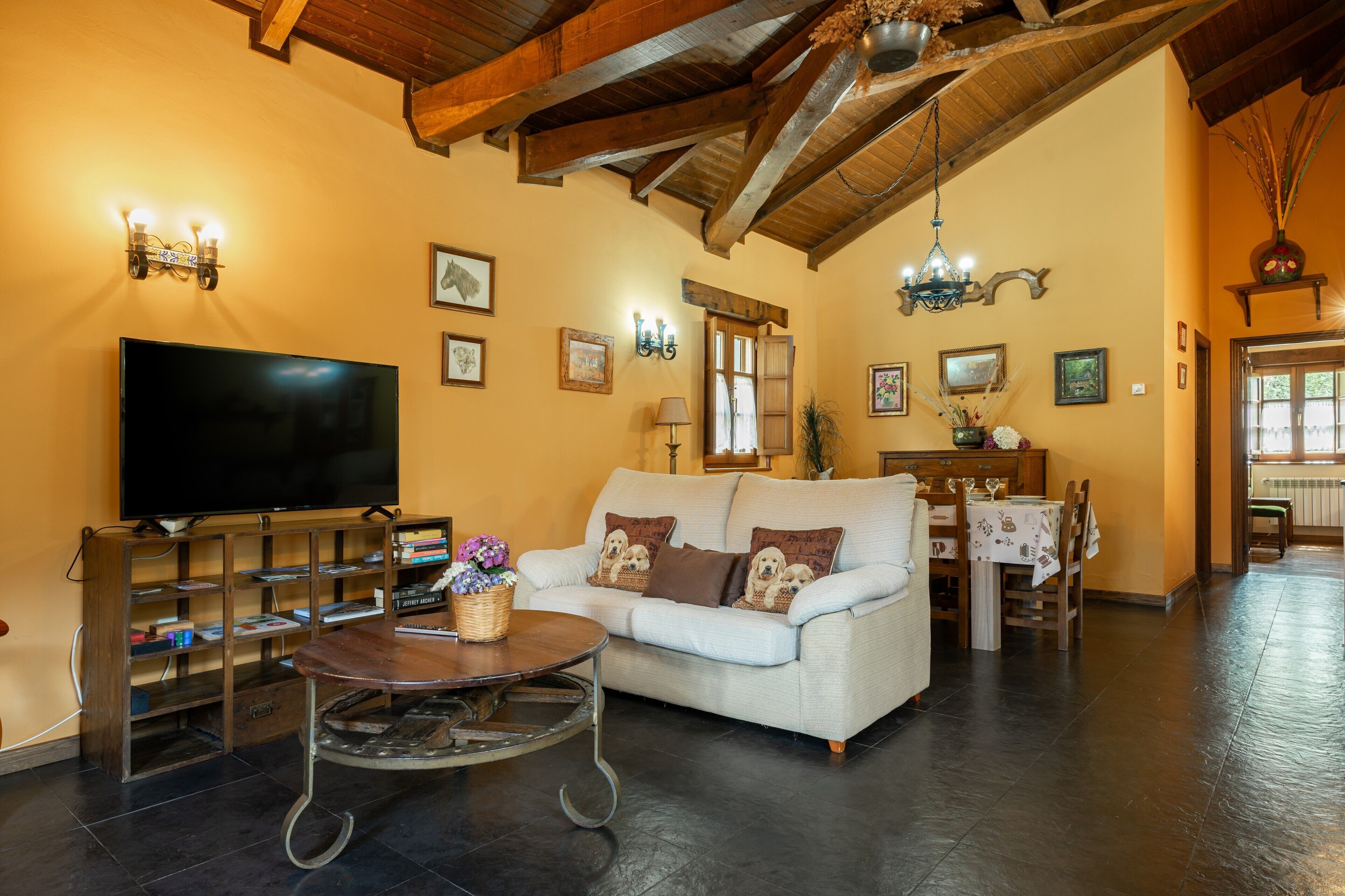 Una sala de estar con sofá, televisor, estantería de madera y un comedor con mesa y sillas.