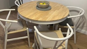 Una mesa de madera redonda con una cesta tejida encima, rodeada por cuatro sillas blancas con asientos de mimbre.