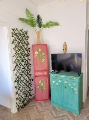 A room with a TV on a teal cabinet, a red cabinet with floral designs, and a green plant on a lattice.