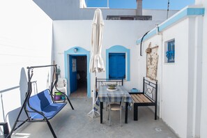 A small outdoor patio with a table, chairs, a swing, and a blue door. - Holiday Home 'Naxos Family House In Vivlos' with Sea View, Wi-Fi and Air Conditioning (Naxos)