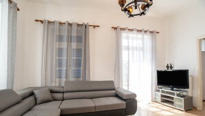 A living room with a sectional sofa, a flat-screen TV on a stand, and a chandelier. - Holiday Home 'Naxos Family House In Vivlos' with Sea View, Wi-Fi and Air Conditioning (Naxos)