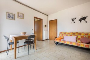 A dining area with a table and chairs, a sofa with cushions, a world map on the wall, and a door leading to another room.