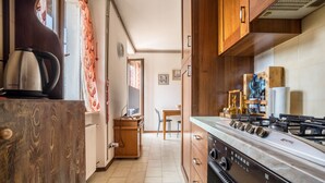 Una cocina compacta con estufa a gas, armarios de madera, un hervidor y un comedor al fondo.