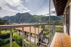 A balcony with a view of mountains, a parked car, and a building with a tiled roof.