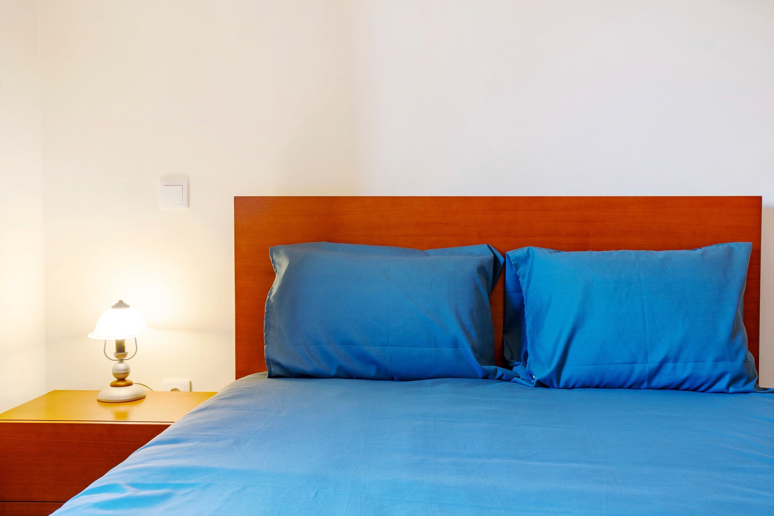 Ein Bett mit blauer Bettwäsche, einem Holz-Kopfteil und einer Nachttischlampe.