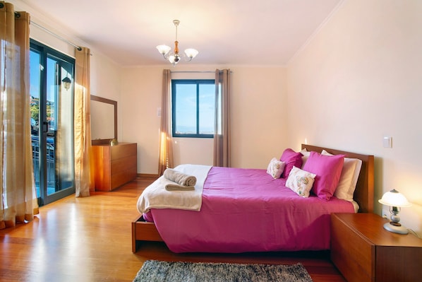 Une chambre à coucher avec un lit, une table de chevet, une lampe, une fenêtre et une vue sur l’extérieur.