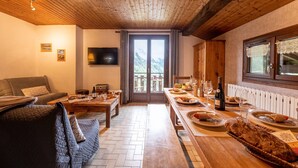 A cozy room with a wooden ceiling, a sofa, a dining table set with plates, glasses, and a bottle. - Apartment 'Chalet Le Grand Nant' with Balcony and Wi-Fi (La Giettaz)