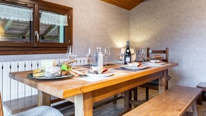 A wooden dining table set with plates, glasses, and a bottle, with a window above and a bench to the right. - Apartment 'Chalet Le Grand Nant' with Balcony and Wi-Fi (La Giettaz)