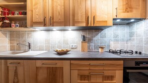 A kitchen with wooden cabinets, a sink, a gas stove, and a tiled backsplash. - Apartment 'Chalet Le Grand Nant' with Balcony and Wi-Fi (La Giettaz)