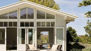 A modern house with large glass windows, a covered patio with two chairs, and a view of a tree and landscape. - Isca House, Exeter, NSW, Isca House, Exeter (Exeter)