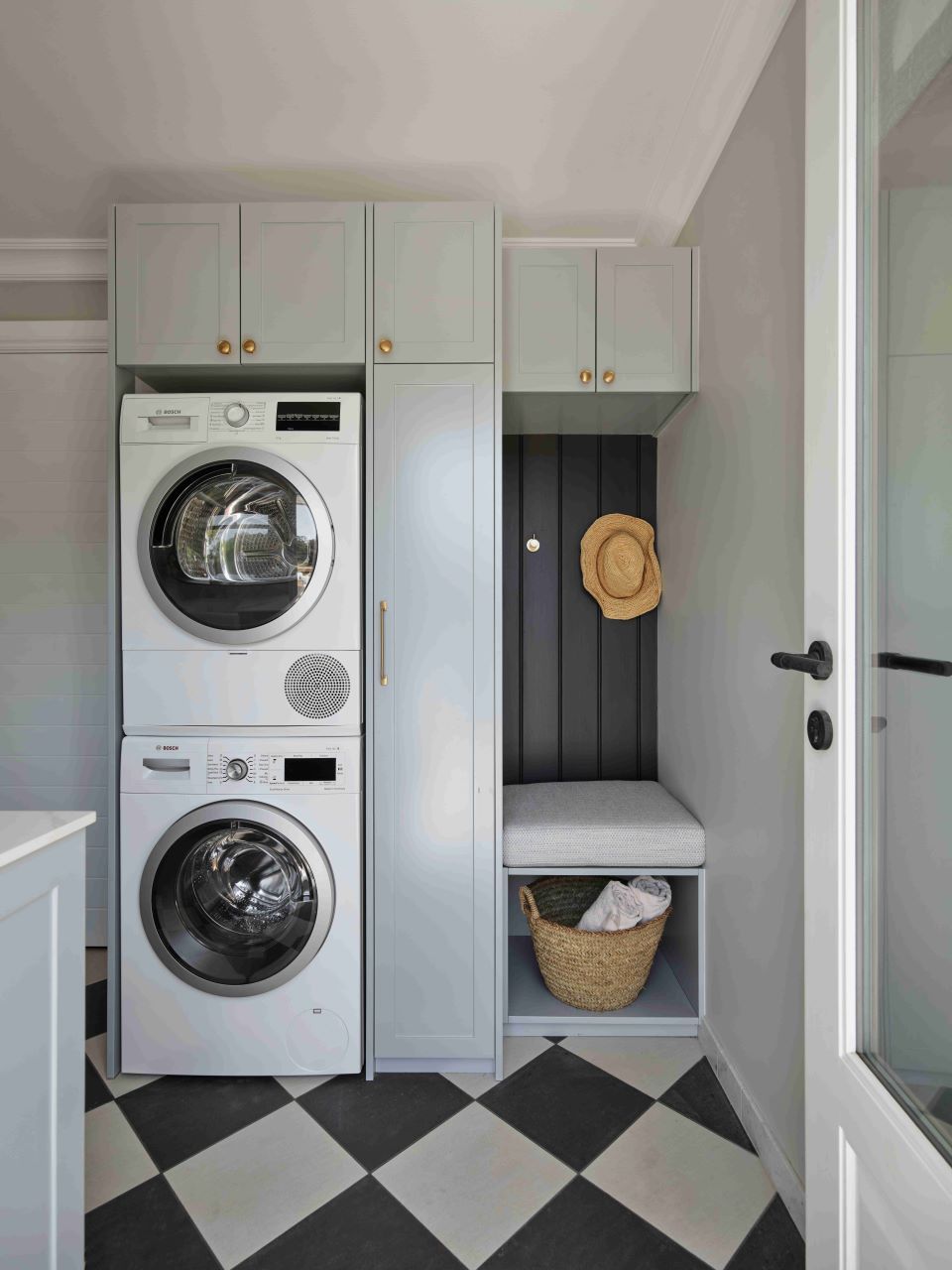 A laundry room with stacked washing machines, a hat on the wall, and a checkered floor.