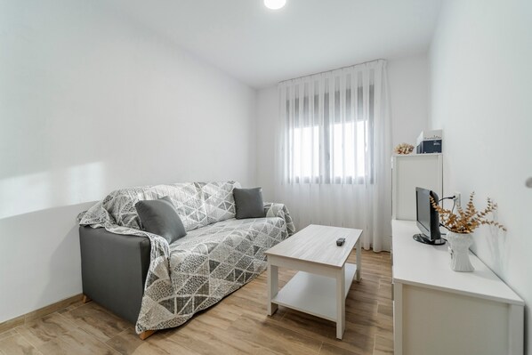 A modern, minimalistic room with a grey sofa, a white coffee table, and a TV on a white stand.
