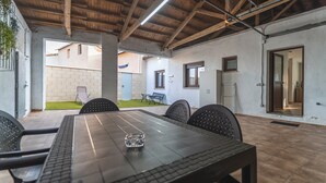 Un patio interior con una mesa larga, sillas y un techo con vigas a la vista.