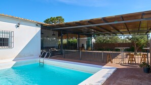 A swimming pool with a covered patio area, a wooden fence, and outdoor furniture.