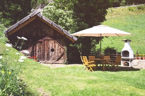 Une cabane en bois rustique, dotée d’une grande porte, d’une table de patio avec des chaises et d’un four à pizza.