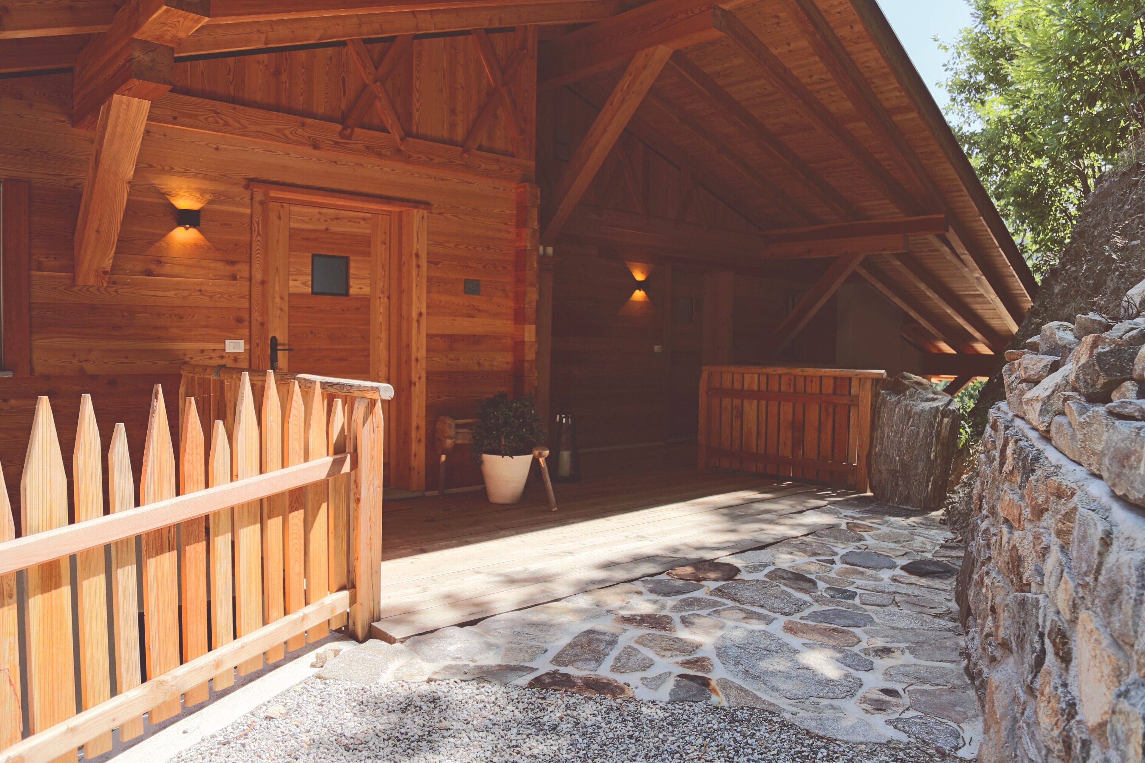 Une cabane en bois avec une entrée pavée de pierres, une clôture en bois et un mur de pierres.