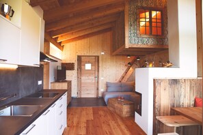 Une cuisine de taille réduite, dotée d’une cuisinière moderne, de meubles blancs et d’un plafond en bois.