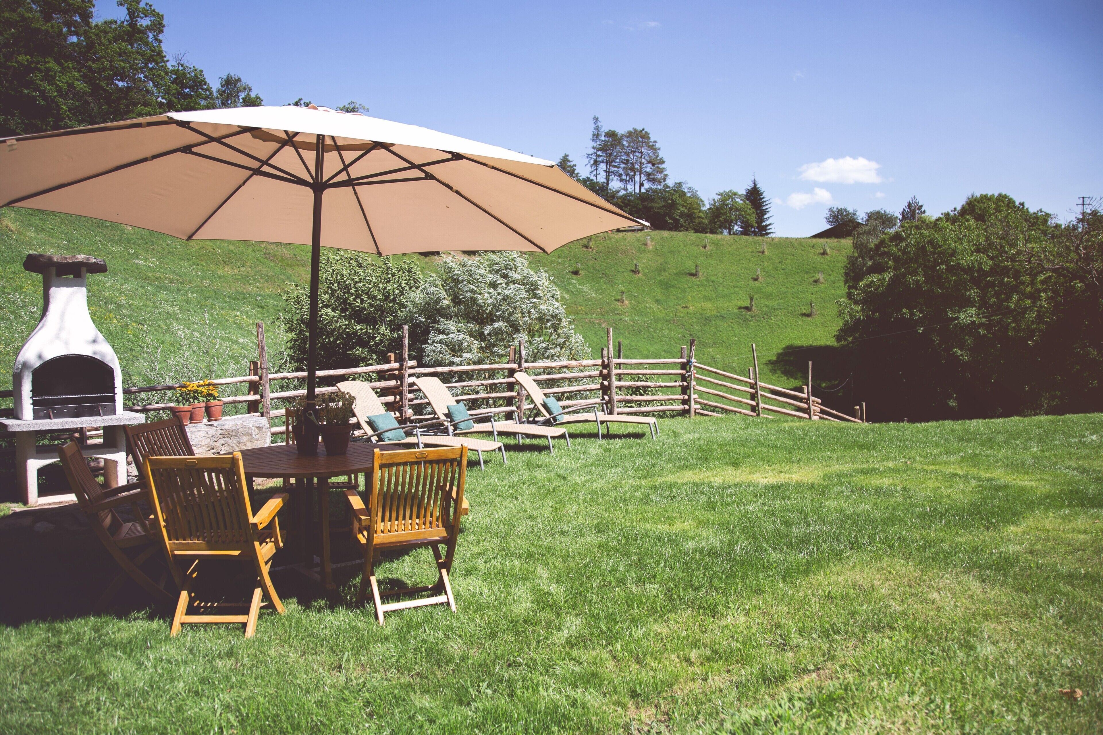 Une terrasse avec un barbecue, des chaises en bois et un parasol.