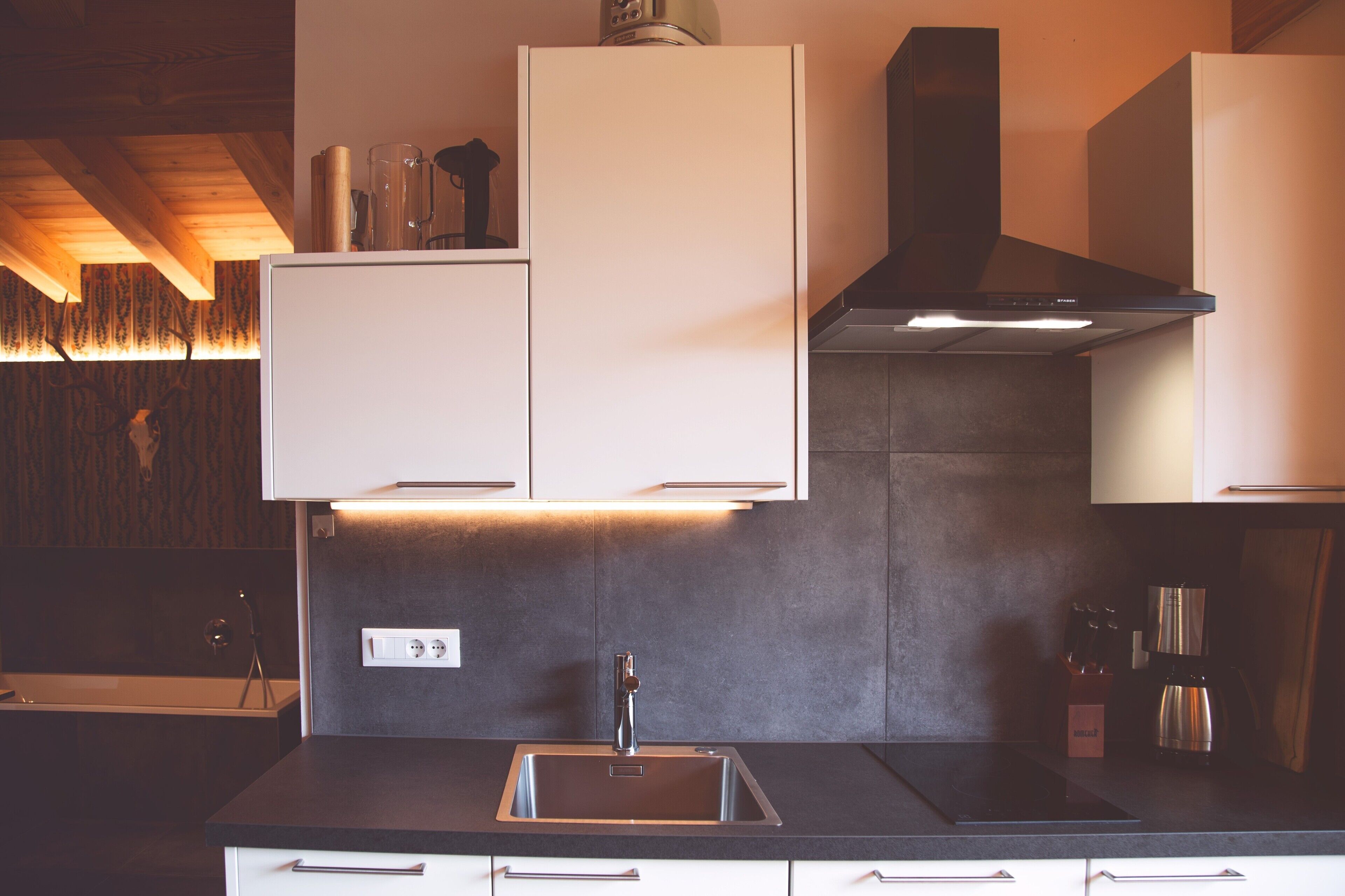 A modern kitchen with a stainless steel sink, white cabinets, and a black range hood.