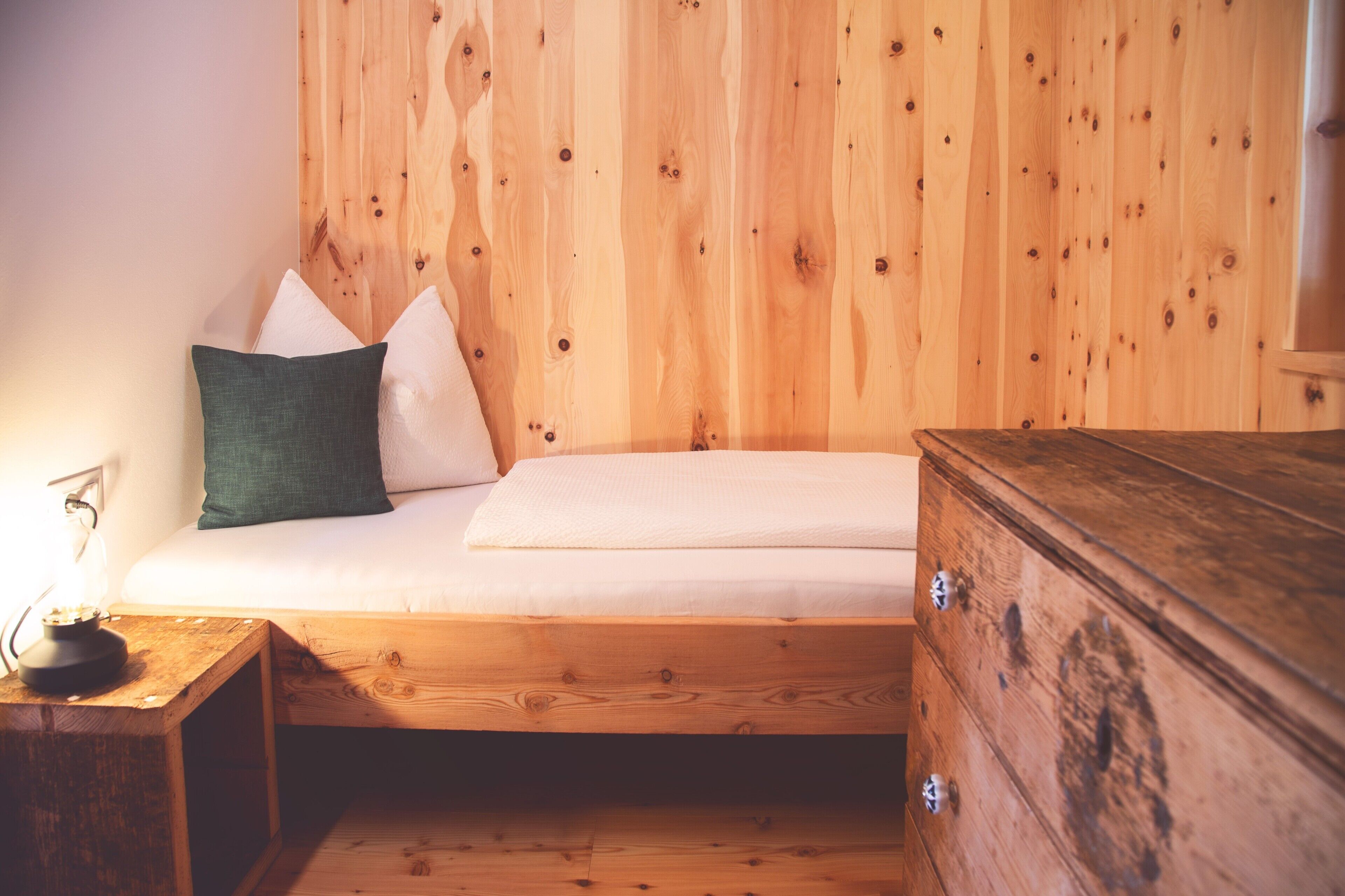Ein Bett mit Kissen, ein Nachttisch und eine Kommode in einem Zimmer mit Holzwänden.