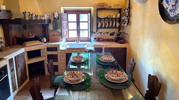Une cuisine avec une table en bois mise pour deux personnes, un évier et divers ustensiles et vaisselle de cuisine.
